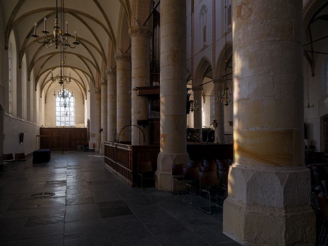 Kircheninnenraum mit Säulen, Bänken und einem Fenster, teils im Schatten.